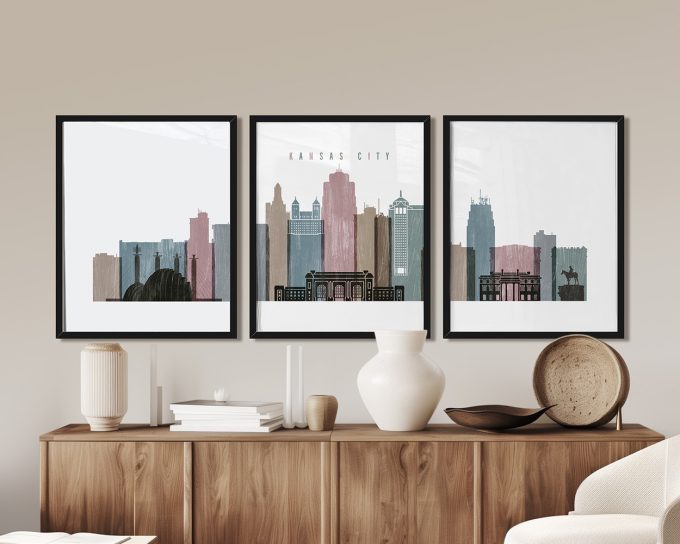Three framed art prints of Kansas City skyline in muted colors displayed on a wooden surface.