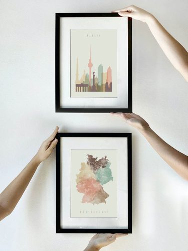 Two framed art prints featuring a silhouette of Berlin and a map of Germany held by hands.