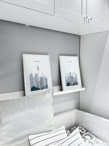 Two framed cityscape prints displayed on a shelf in a room with light gray walls.