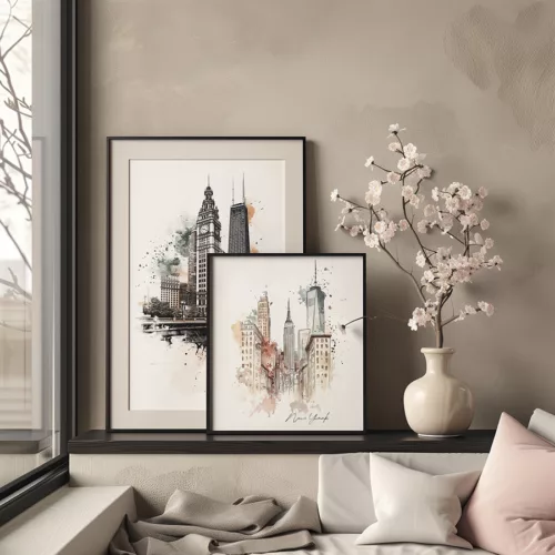 Two framed cityscape art prints of New York City displayed on a shelf with a vase and flowers.