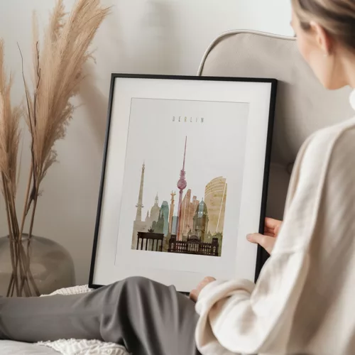 Person holding a framed print of a Berlin cityscape featuring notable buildings and landmarks.