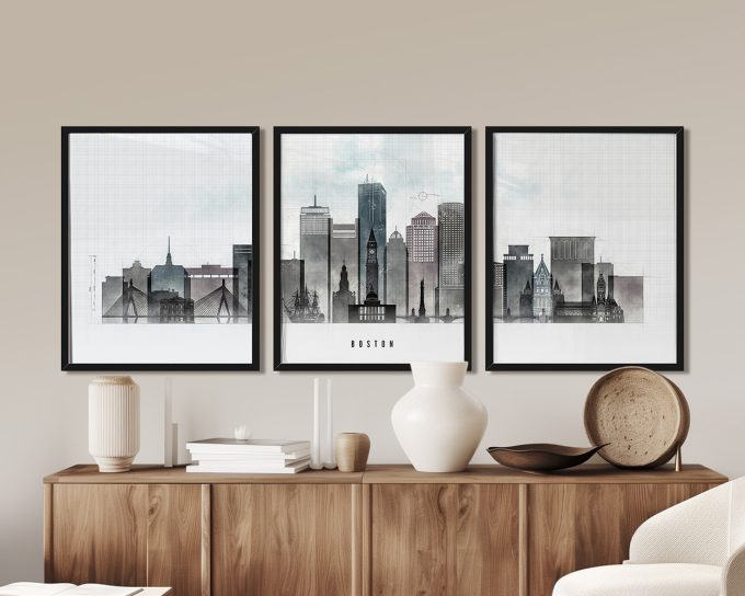 Three framed art prints of Boston's skyline displayed on a wooden surface.