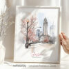 Hand holding a framed art print of Boston in watercolor drawing with soft pastel tones.