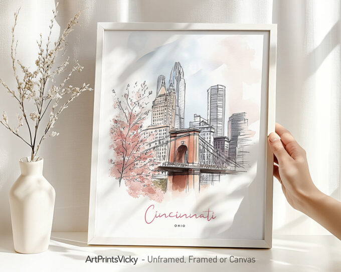 Hand holding a framed art print of Cincinnati in watercolor drawing with soft pastel tones.