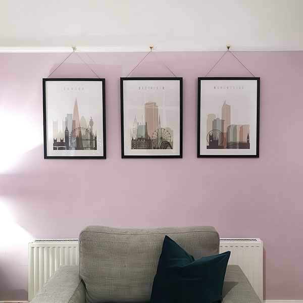 Three framed cityscape prints of London, Edinburgh, and Manchester hanging on a wall.