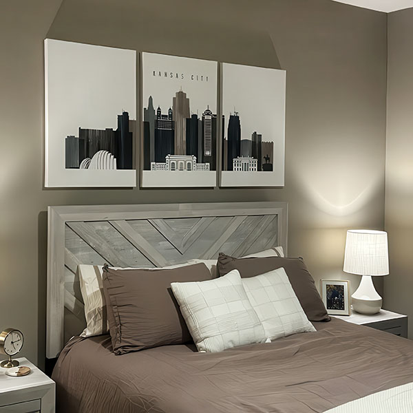 Three-panel artwork depicting the skyline of Kansas City in neutral colors above a bed with gray bedding.