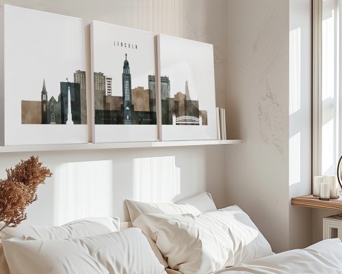 Three art prints depicting a cityscape of Lincoln displayed above a bed in a room.
