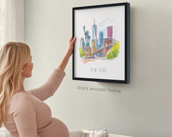 Pregnant woman adjusting a framed illustration of New York City on a wall.