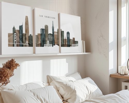 Three art prints of a San Francisco cityscape displayed on a shelf above a bed with white bedding.