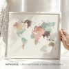 Art print of a world map with watercolor effects in various colors, framed and held by a hand.