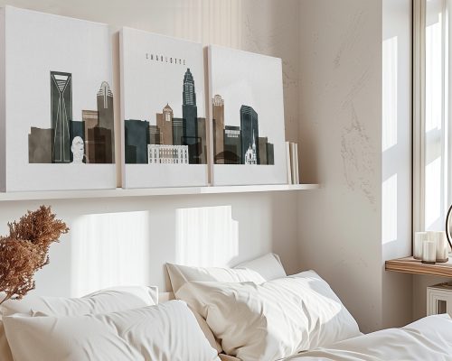 Three framed art prints depicting the skyline of Charlotte, North Carolina, displayed above a bed.
