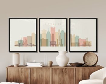 Three framed art prints depicting a stylized skyline of Pittsburgh with various buildings and bridges.