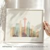 Framed artwork depicting a stylized cityscape of Seattle with notable buildings and the Space Needle.