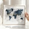 A world map illustration in blue tones displayed in a white frame held by a hand.